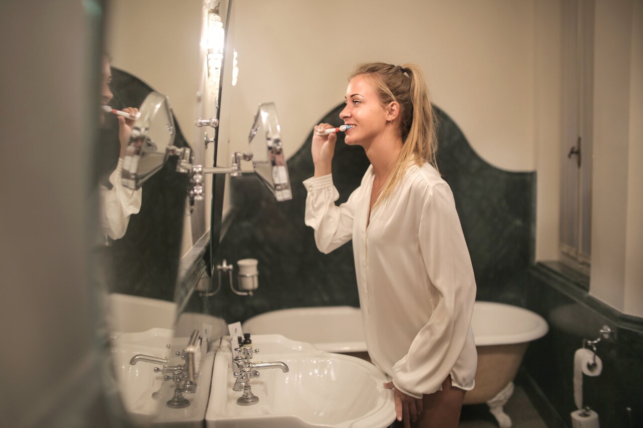 woman brushing teeth in front of a mirror