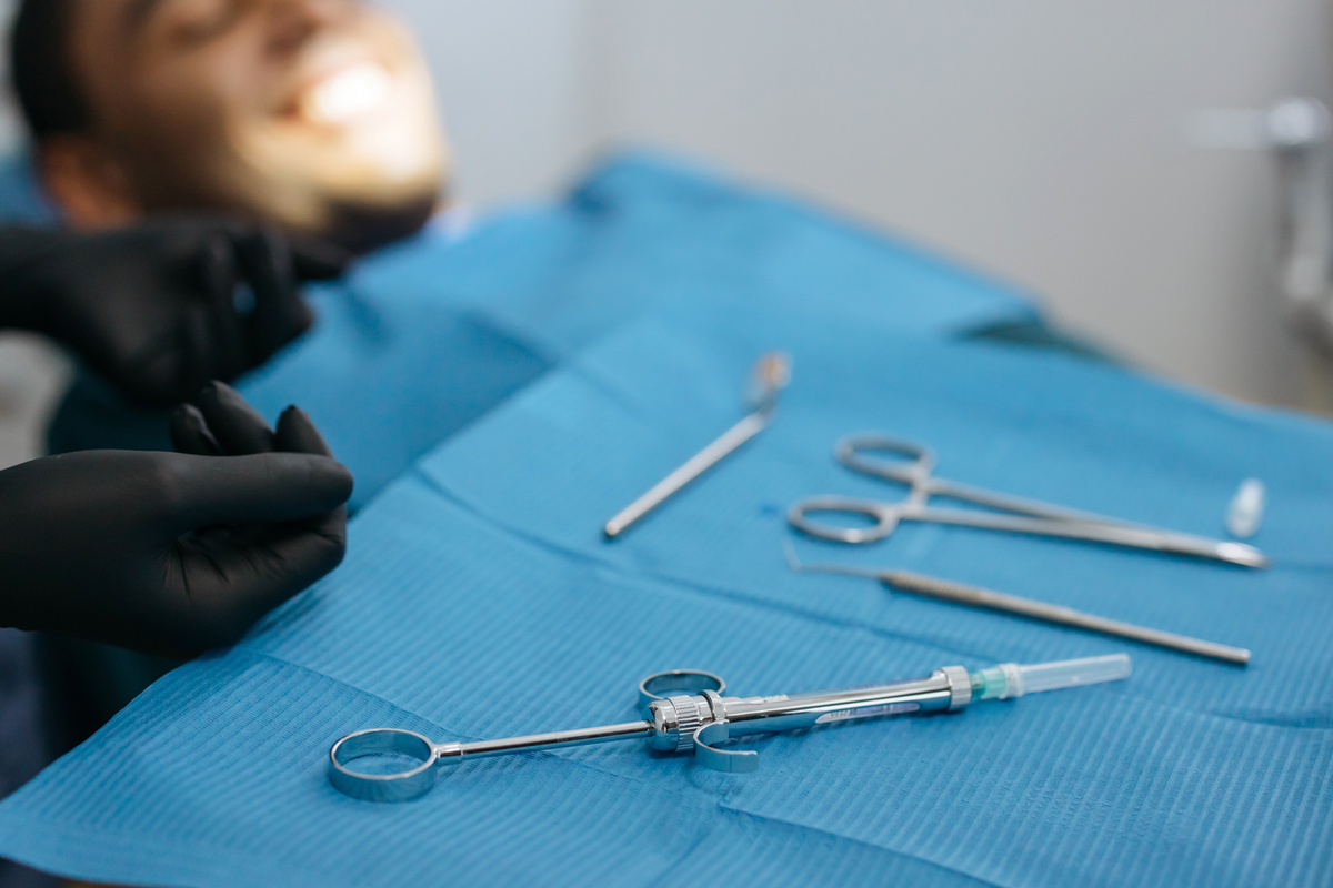 Young man waiting in dentist chair for procedure while dentist's hand uses dental tools